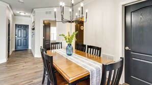 Een eethoek met een houten tafel, zwarte stoelen, een vaas met bloemen en een zwarte kroonluchter.