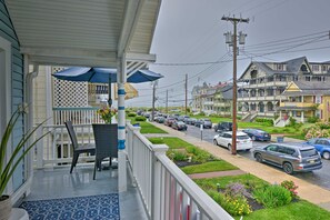A porch with a chair and umbrella, overlooking a street with parked cars and houses. - Ocean Grove Apt. w/ Balcony: 1 Block to the Beach! (Ocean Grove)