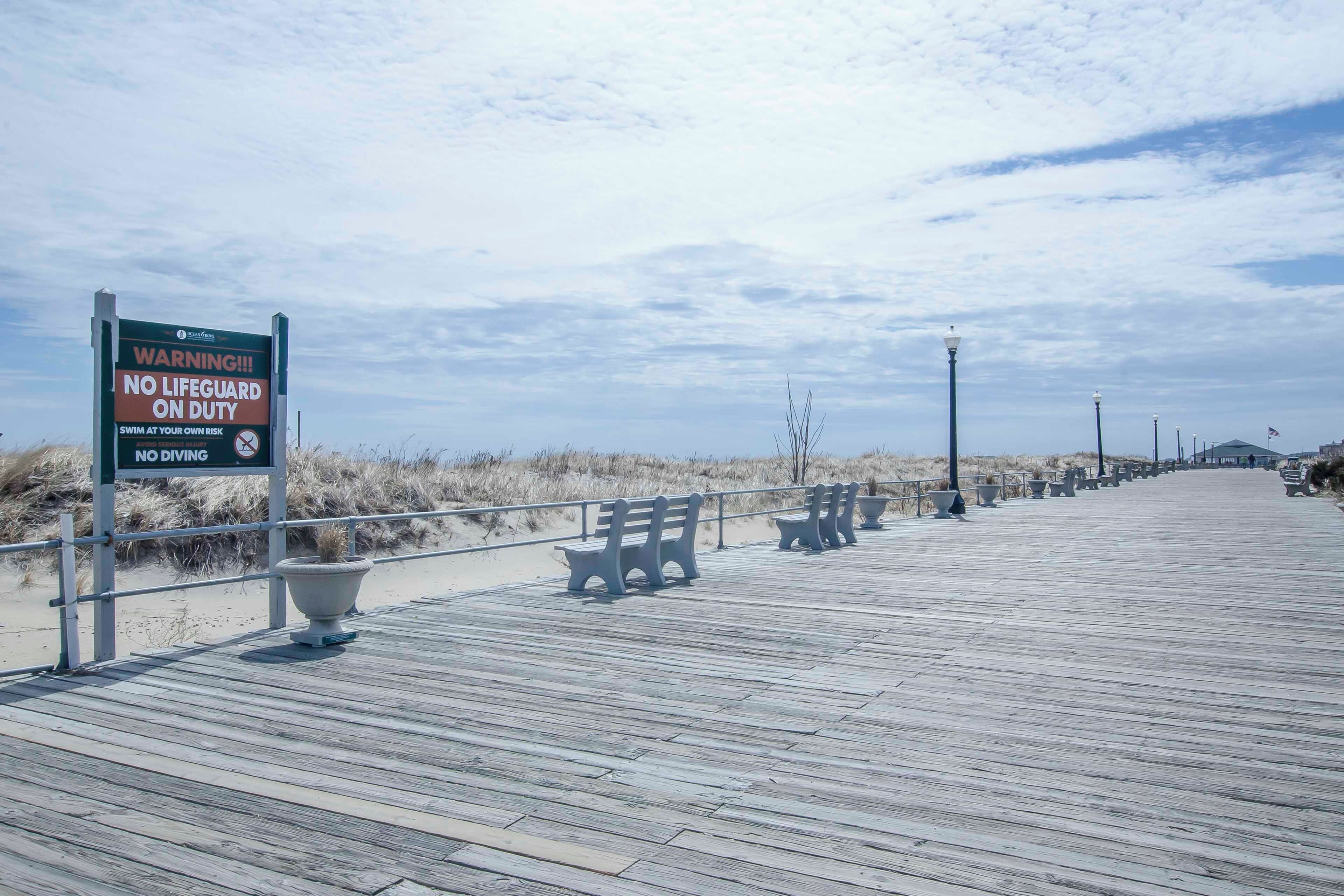 A wooden boardwalk with benches and a warning sign about no lifeguard on duty.