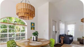 A dining area with a round table, green chairs, and a hanging wicker light fixture. - Stylish Coastal Retreat Home (West Palm Beach)
