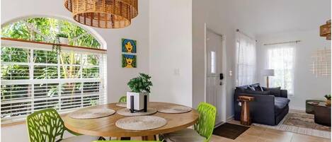 A dining area with a round table, green chairs, and a hanging wicker light fixture.