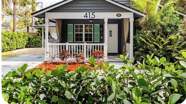 A house with the number 415, a porch with a white railing, and a small garden area with red mulch. - Stylish Coastal Retreat Home (West Palm Beach)