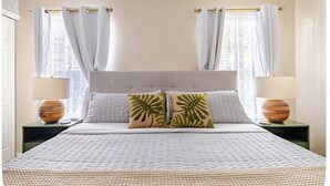 A bed with a headboard, two pillows with leaf patterns, and two bedside lamps on nightstands. - Stylish Coastal Retreat Home (West Palm Beach)