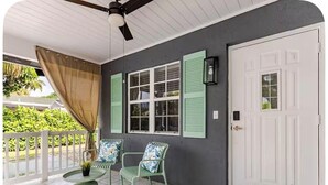 A covered porch with a ceiling fan, a white door, and two chairs with patterned cushions. - Stylish Coastal Retreat Home (West Palm Beach)