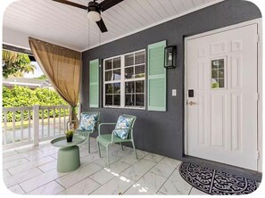 A covered porch with a ceiling fan, a white door, and two chairs with patterned cushions.
