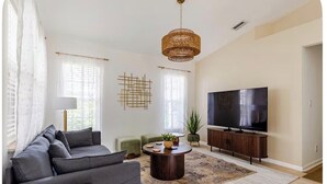 A living room with a sofa, a coffee table, a TV, and a hanging light fixture. - Stylish Coastal Retreat Home (West Palm Beach)
