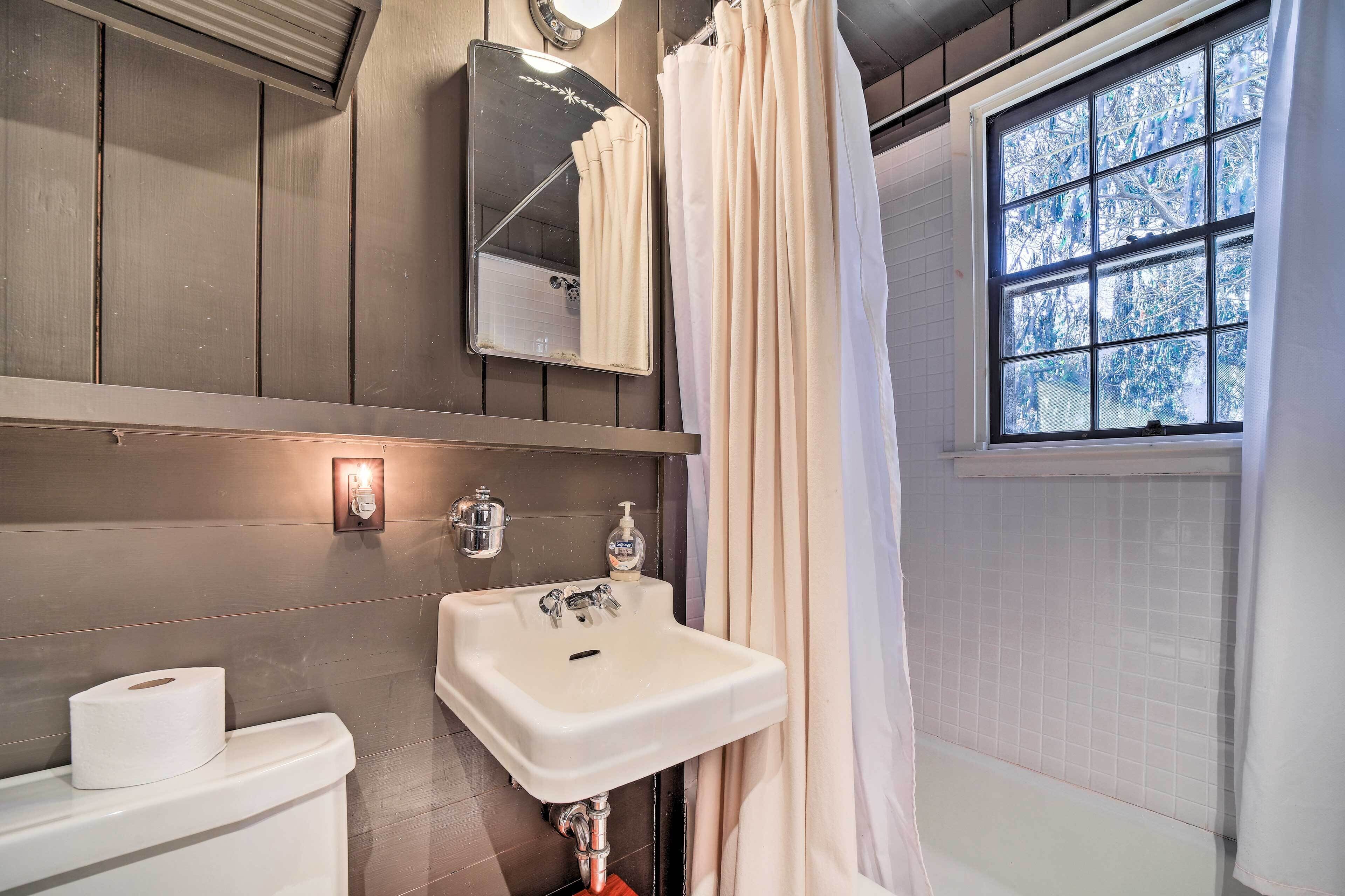 A bathroom with a white sink, a mirror, a toilet, and a window with a view of trees.