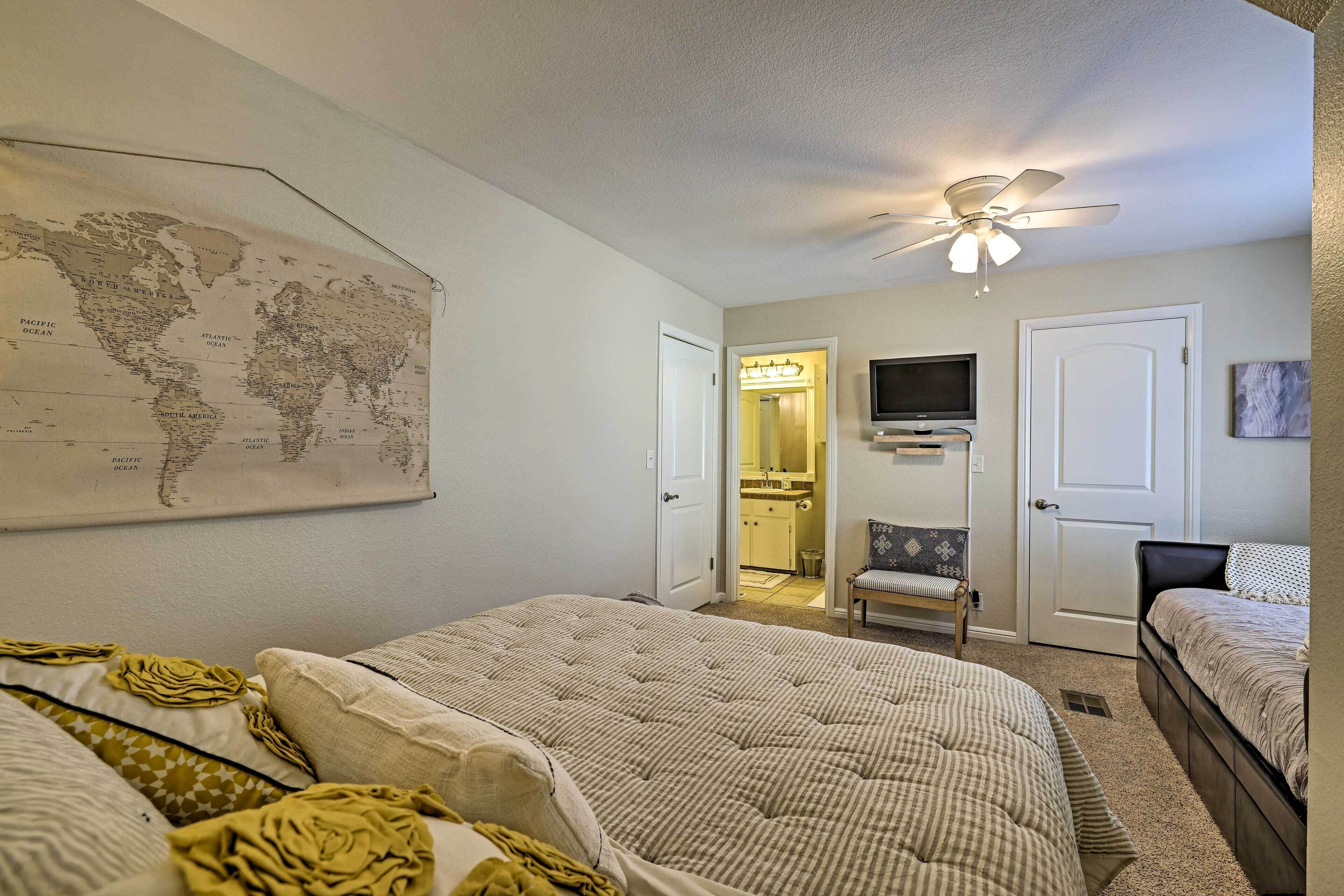 Une chambre avec deux lits, une carte du monde accrochée au mur, un ventilateur de plafond et un téléviseur.
