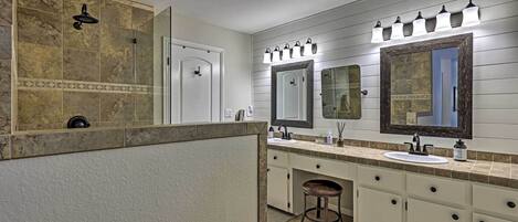 A bathroom with a large mirror, two sinks, a shower, and a vanity with a stool.