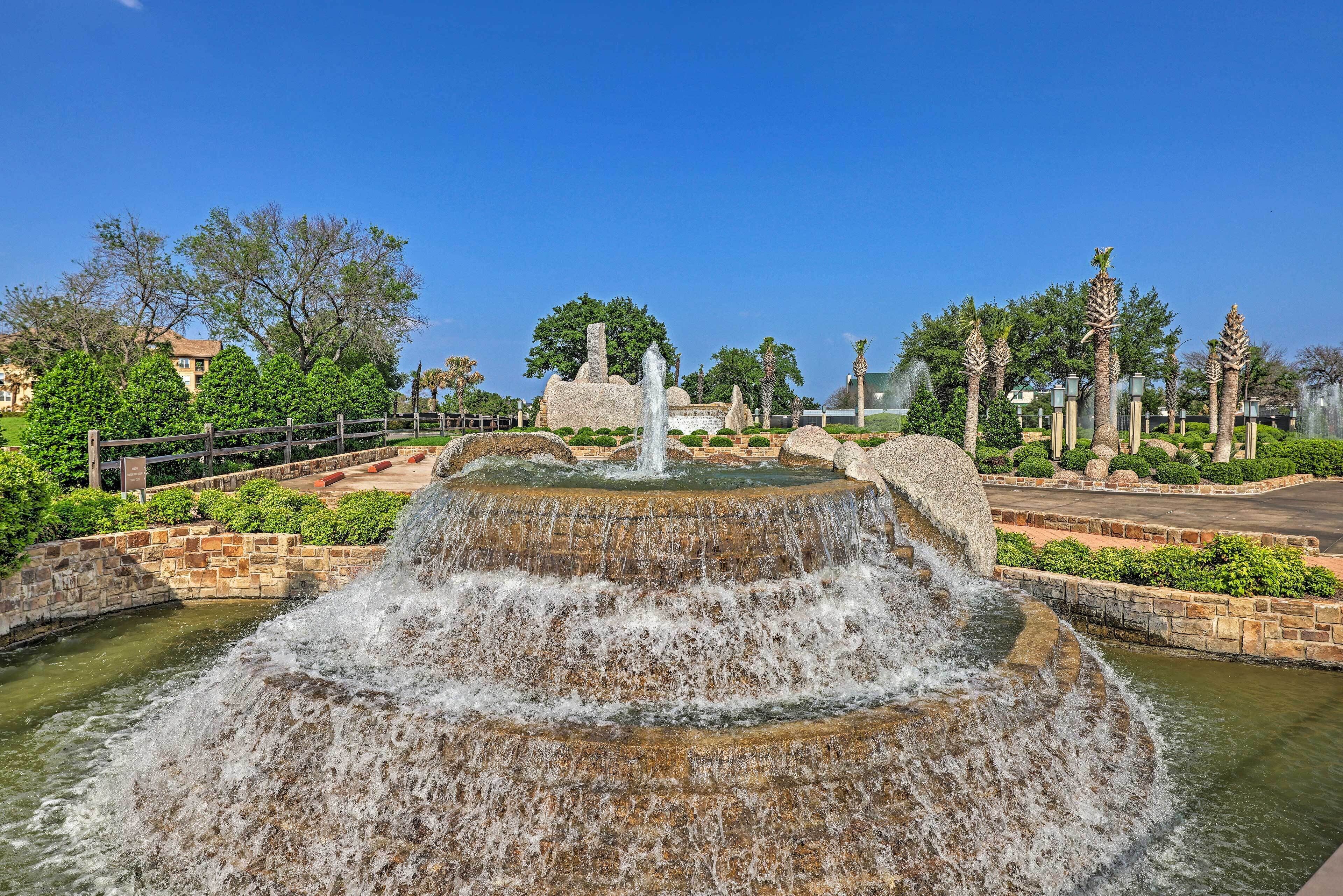 A multi-tiered water fountain with cascading water, surrounded by stone walls and palm trees.