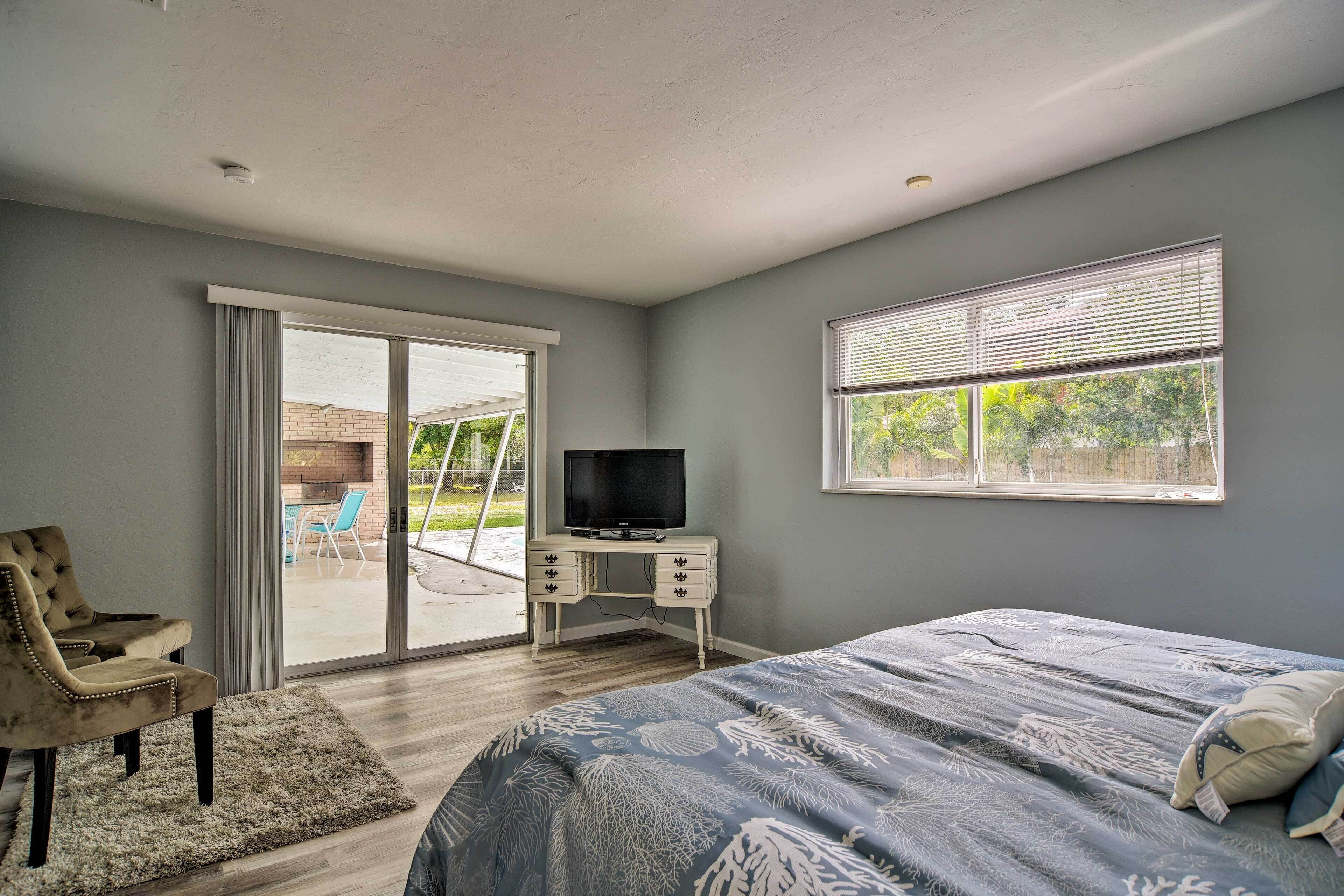 A bedroom with a bed, a TV on a dresser, a chair, and a sliding glass door leading to an outdoor area.
