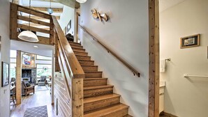 Un escalier en bois avec une rampe, une cheminée en pierre et une vue sur un salon comprenant un canapé et une autre cheminée.