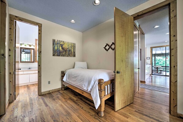 A bedroom with a wooden bed, a painting on the wall, and a view of the outdoors through a door.