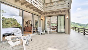 Une vaste terrasse extérieure dotée d’un plancher en bois, de chaises en plastique blanches et d’une porte vitrée donnant sur une pièce intérieure avec un canapé et une table à manger.