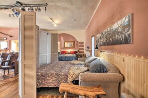 Une chambre confortable avec un grand lit, un canapé et un banc en bois. On aperçoit à l’arrière-plan un coin repas avec des chaises et une table.