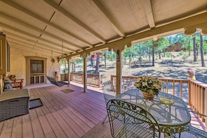 A covered outdoor area with a wooden deck, metal chairs, a table with a basket of flowers, and a hammock. - House of Angels Retreat w/ Deck Near Winter Park (Ruidoso)