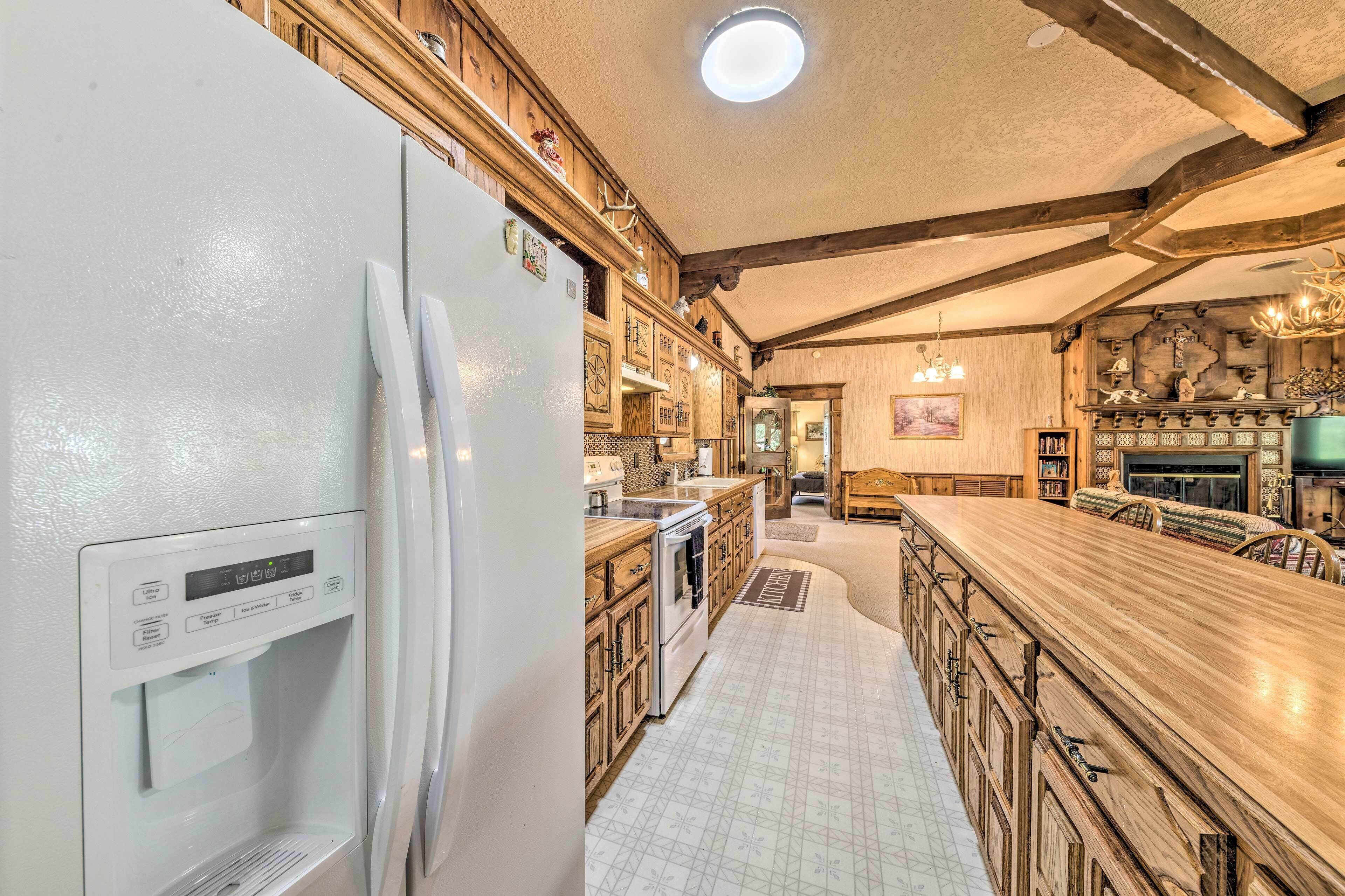 A kitchen with a built-in refrigerator, wooden cabinets, a large island with bar stools, and a stone fireplace.