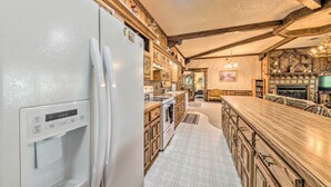 A kitchen with a built-in refrigerator, wooden cabinets, a large island with bar stools, and a stone fireplace. - House of Angels Retreat w/ Deck Near Winter Park (Ruidoso)