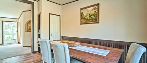 A dining area with a wooden table and four chairs, a painting on the wall, and a door leading to another room.