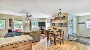 A spacious living room with a sofa, dining table, and chairs. There is a TV mounted on the wall and a ceiling fan. - Sunny Morristown Home - Walk to Restaurants! (Morrisville)