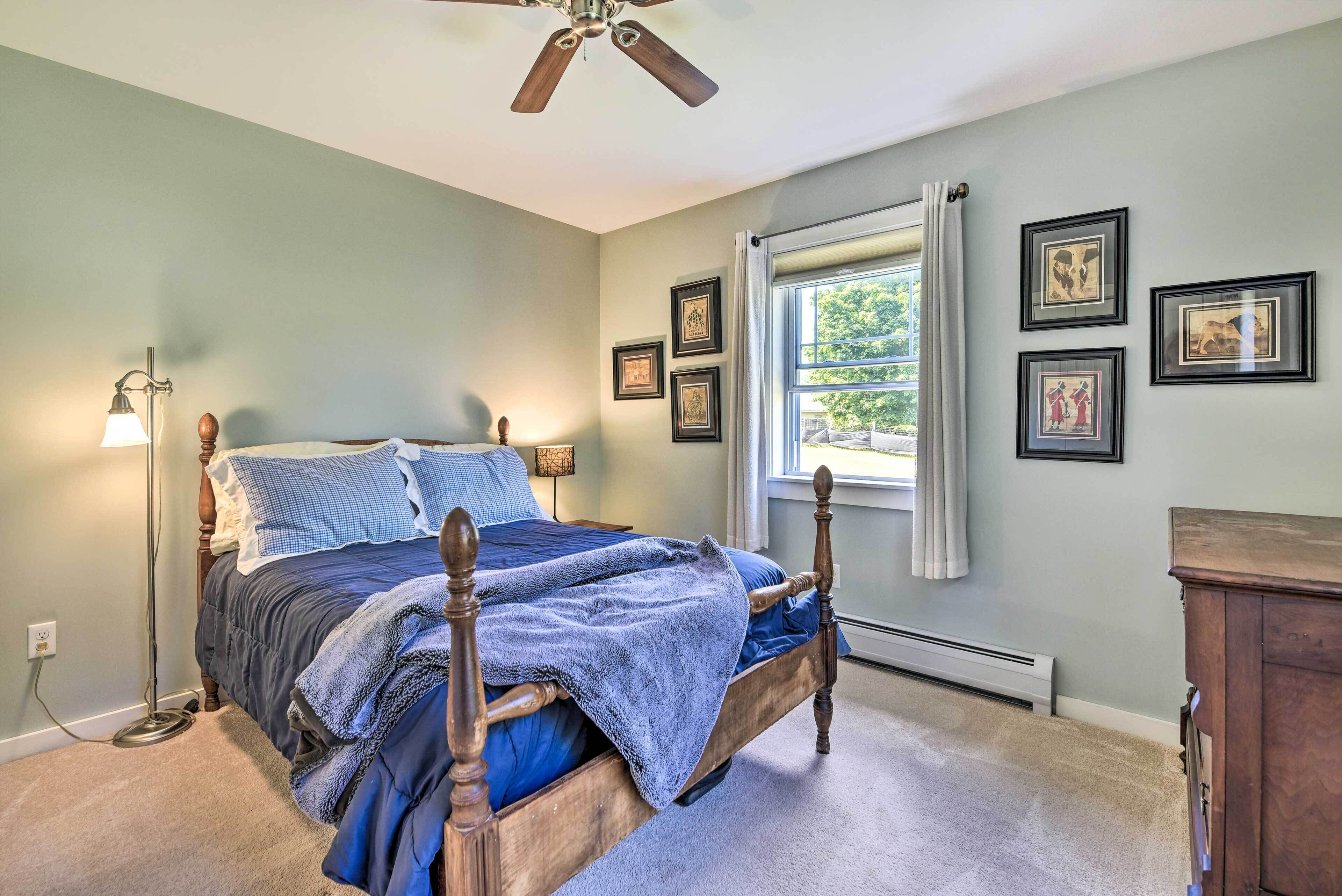 Une chambre avec un lit en bois, un ventilateur de plafond, une fenêtre avec des rideaux et des tableaux encadrés accrochés au mur.