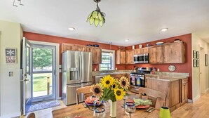 A modern kitchen with wooden cabinets, stainless steel appliances, and a dining area with a table set for four. - Sunny Morristown Home - Walk to Restaurants! (Morrisville)