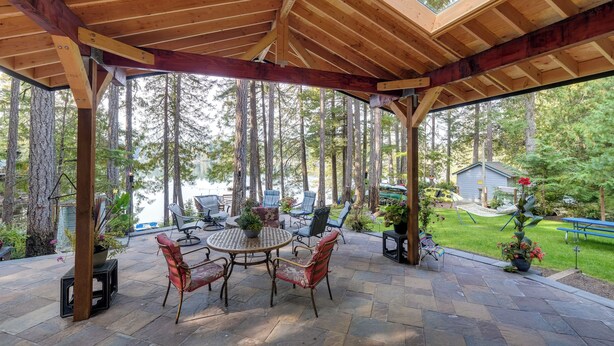 Ein überdachter Patio-Bereich mit Holzboden, Steinfliesen und Gartenmöbeln.