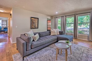 A living room with a grey sectional sofa, a small round table with a plant, and a large window with curtains. - Dog-friendly Bella Vista Home w/ Grill + Deck (Bella Vista)