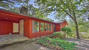 A red wooden house with a stone chimney, large windows, and a covered porch.