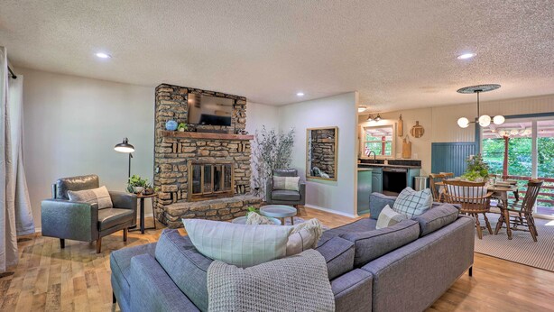 A living room with a stone fireplace, a gray sectional sofa, and a dining area with a round table and chairs.