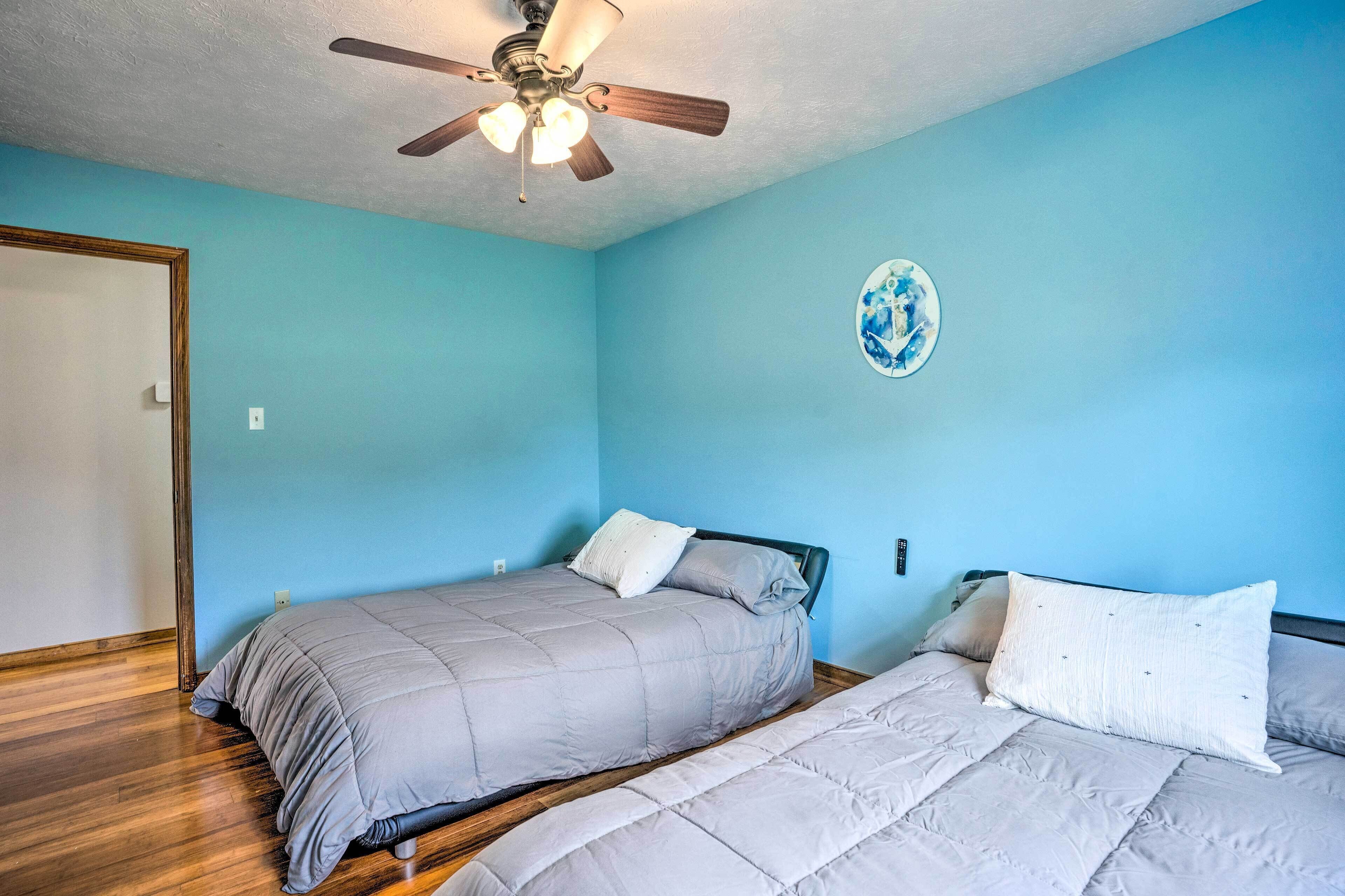 A bedroom with two beds, a ceiling fan, and a wall decoration.