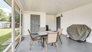 Eine überdachte Terrasse mit Tisch, Stühlen, einem Grill und einer zur Außenseite führenden Tür.