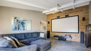 A modern living room with a sectional sofa, ottoman, and a large flat-screen TV mounted on a wooden wall. - Theater Room & Pool Deck: Retreat in Palm Desert! (Palm Desert)