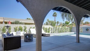 An outdoor patio with a pool, covered seating area, and a stone fire pit. - Theater Room & Pool Deck: Retreat in Palm Desert! (Palm Desert)