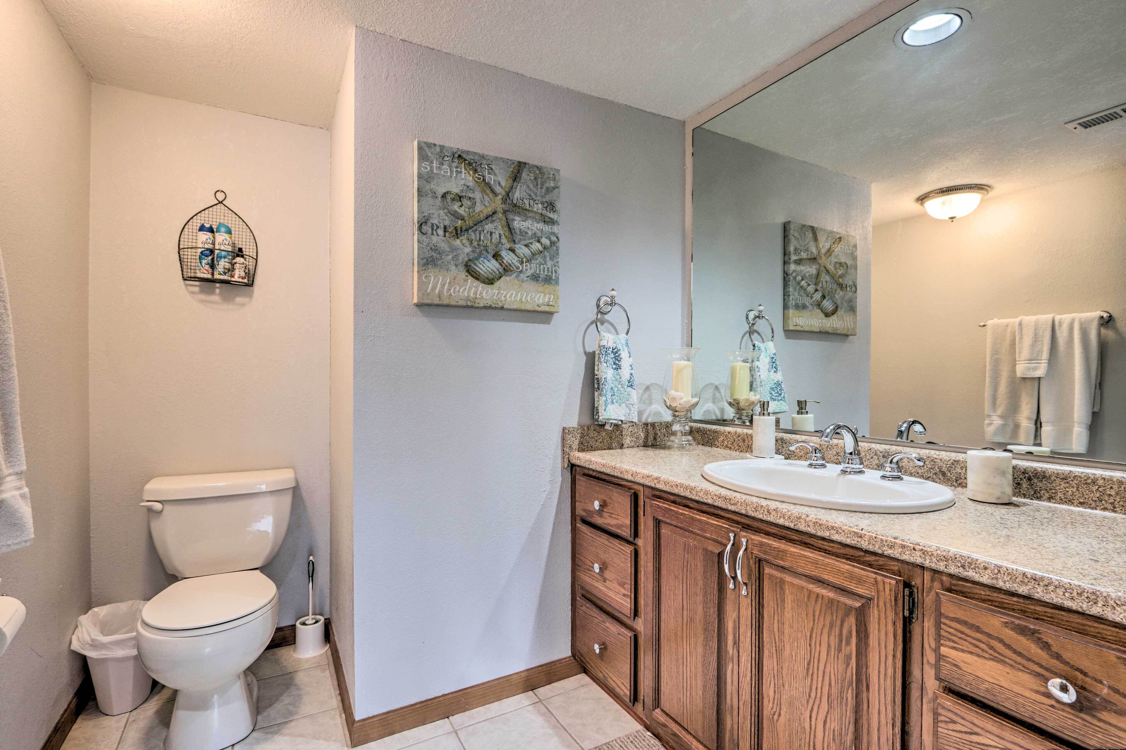 Un baño con inodoro, lavamanos, armarios de madera y decoración en la pared.