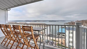 Un balcón con sillas y una mesa de madera, con vista al agua y edificios.