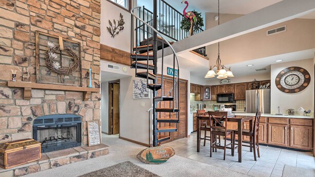Amplia sala de estar con chimenea de piedra, una escalera de madera y una cocina con muebles de madera y electrodomésticos de acero inoxidable.