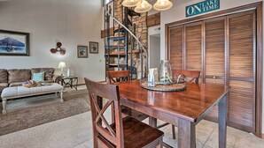 Un comedor con una mesa de madera, sillas y una araña. Se observa una escalera con vistas al exterior.