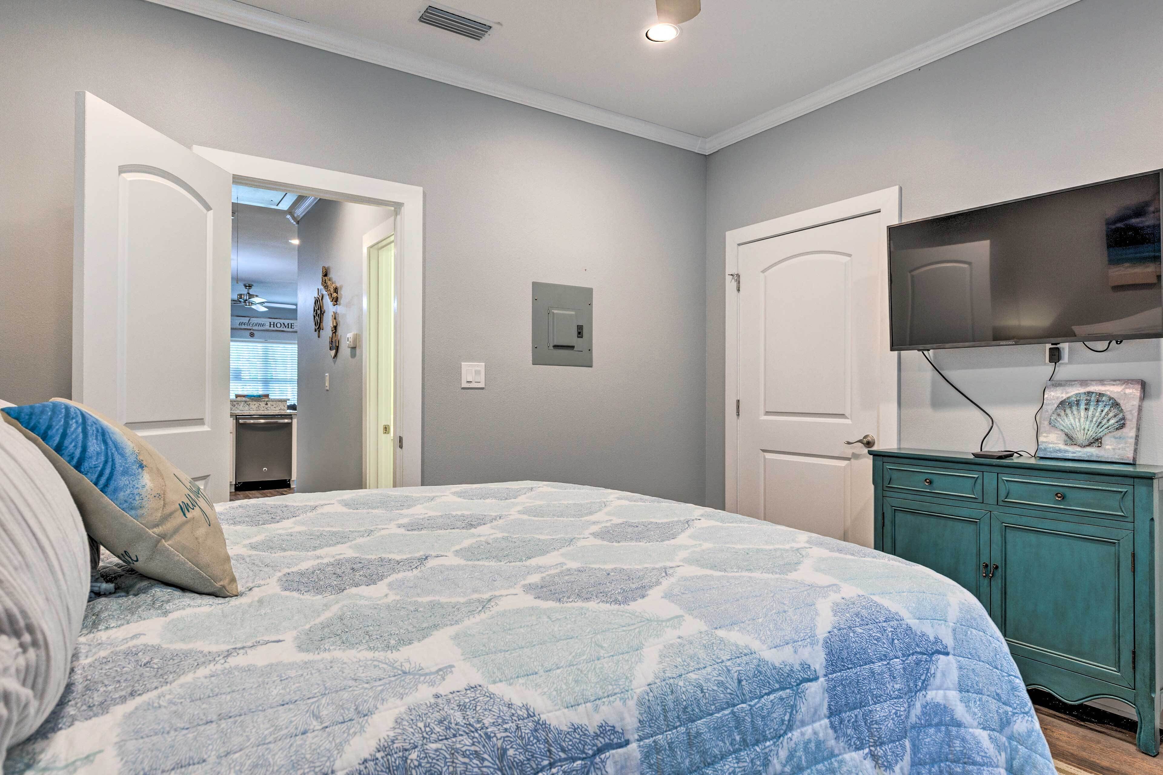 Un dormitorio con una cama, un televisor montado en la pared y una puerta que da a otra habitación.