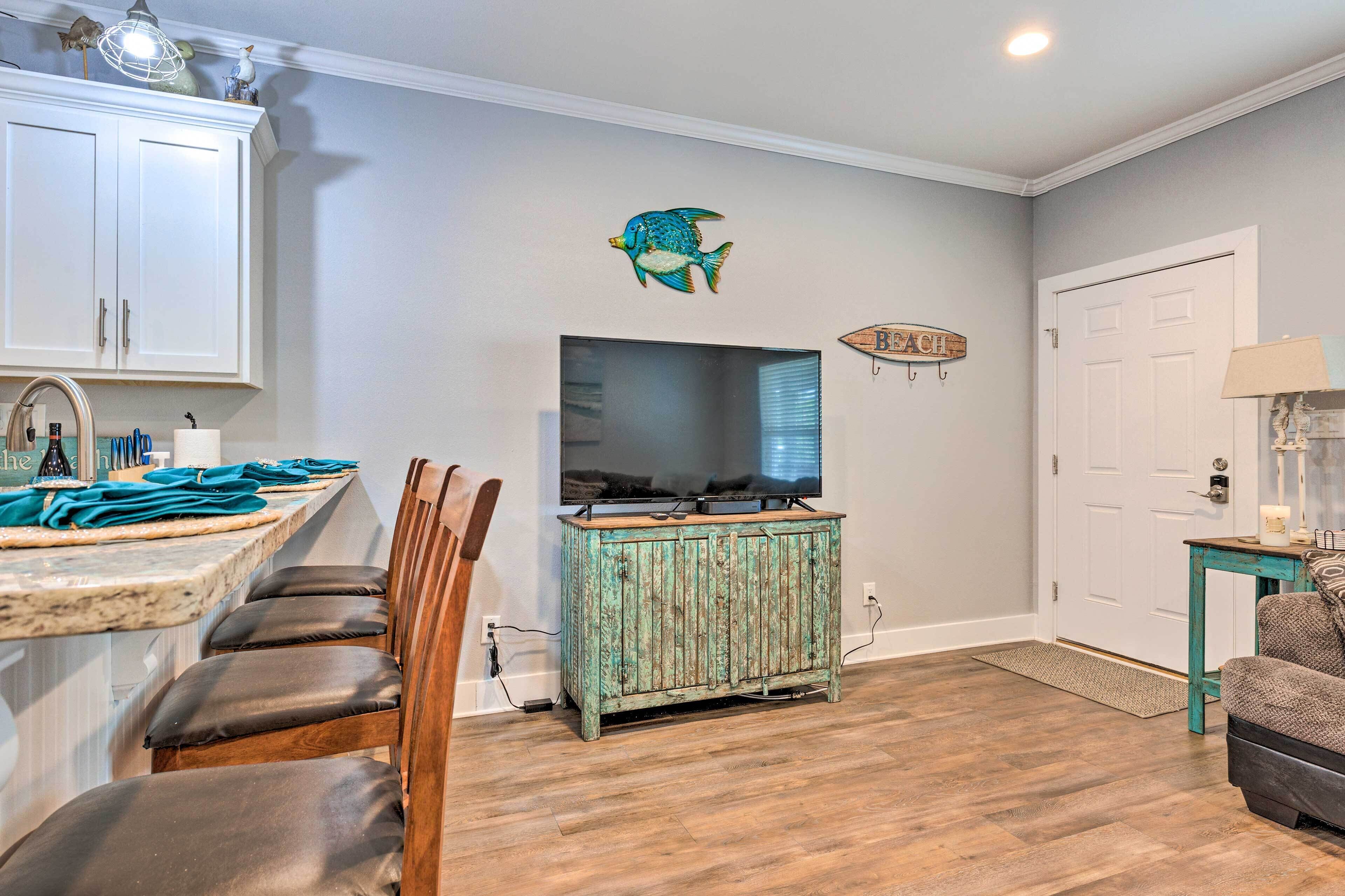 A kitchen with a wooden cabinet, a dining area with chairs, a television, and a fish wall decoration.
