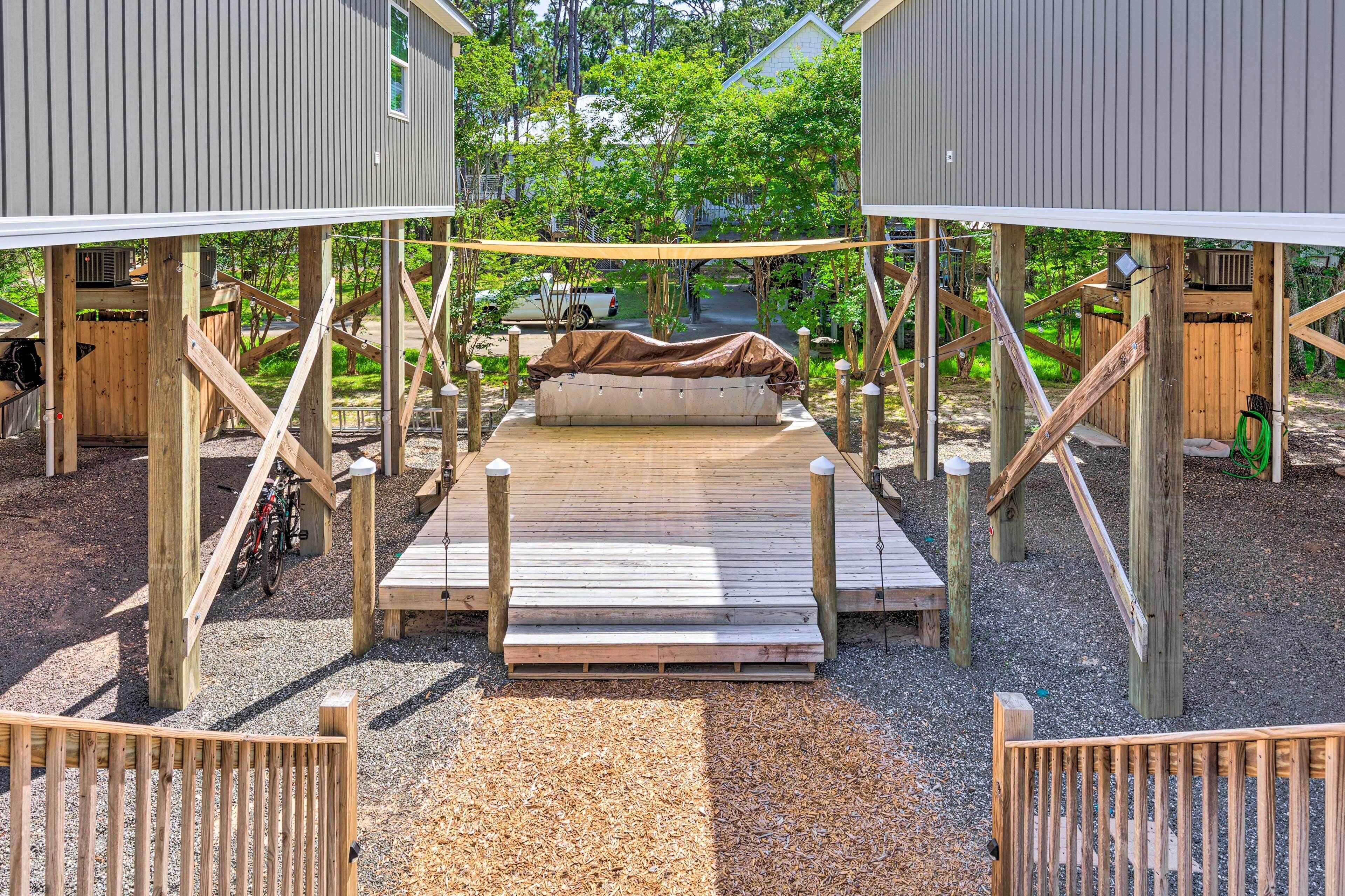 Una terraza de madera con un área de estar techada, rodeada de construcciones de madera y grava.