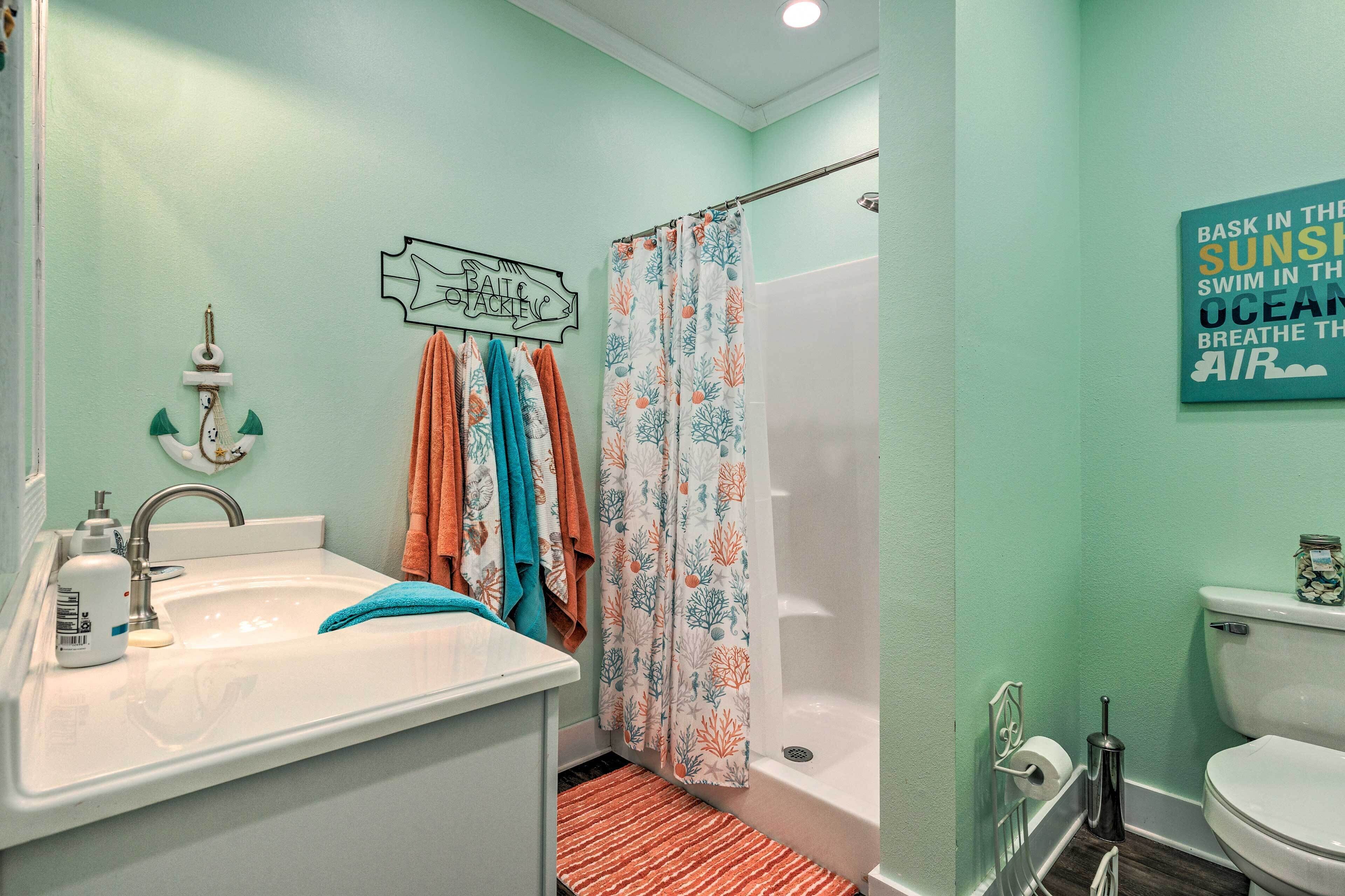 A bathroom with a sink, toilet, and shower. There are towels hanging on the wall and a sign with a nautical theme.