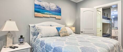 A bedroom with a bed, nightstand, lamp, and a painting of a beach scene.