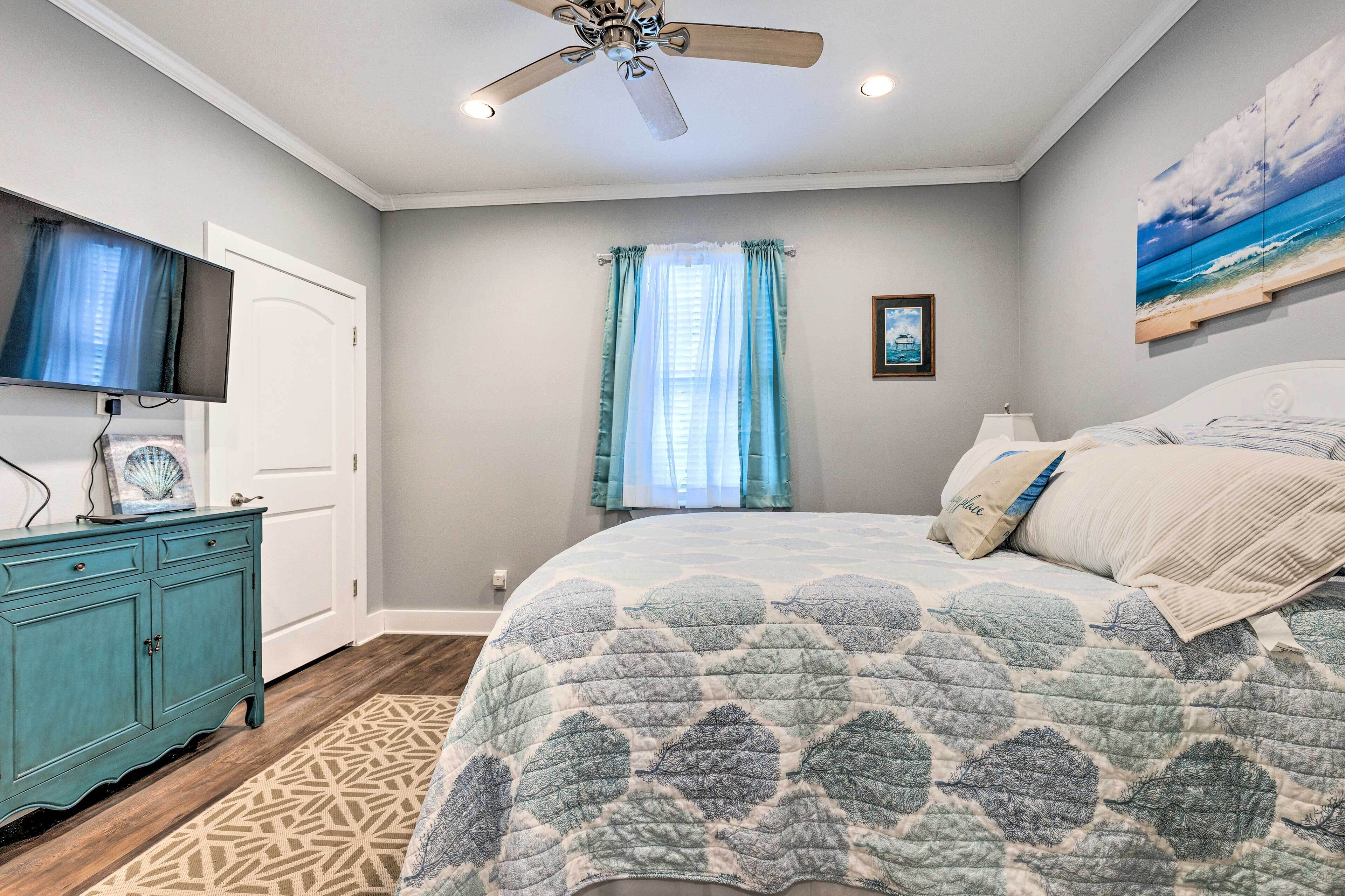 A bedroom with a bed, a ceiling fan, a TV, a dresser, and a window with curtains.