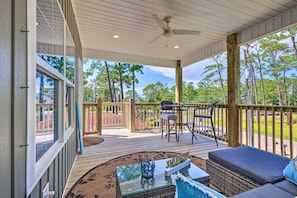 A covered outdoor deck with a table and chairs, a sofa, and a view of trees.