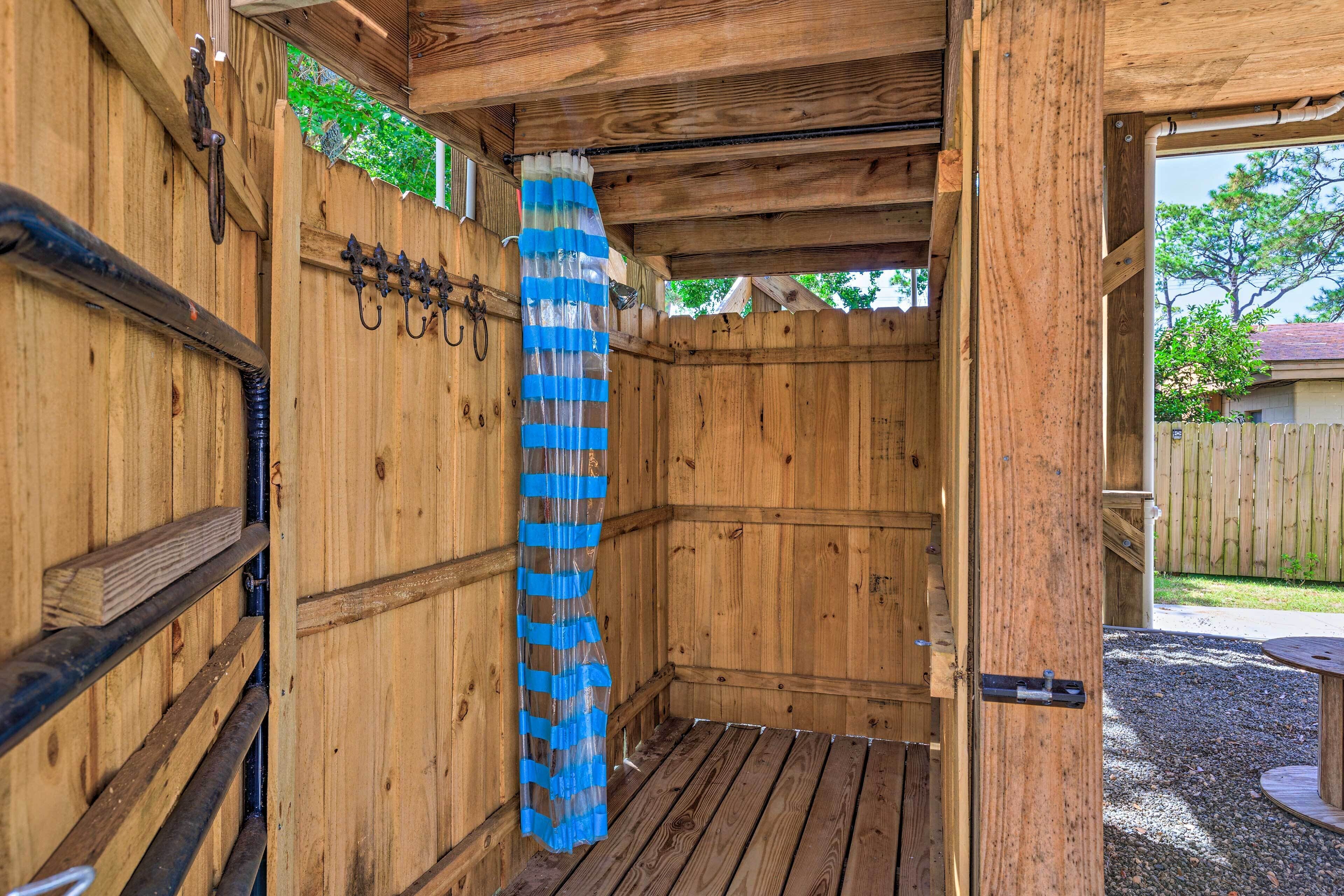 Un espace de douche extérieur en bois, doté d’une porte en bois, d’une poignée en métal et d’un rideau de douche bleu.
