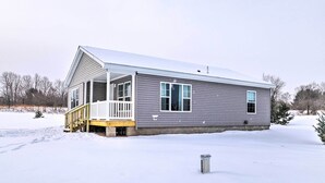 Una casa de un piso con porche cubierto y una pequeña terraza, rodeada de nieve.
