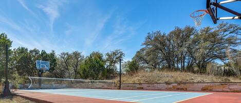 An outdoor basketball court with a blue playing surface, a basketball hoop, and a net.