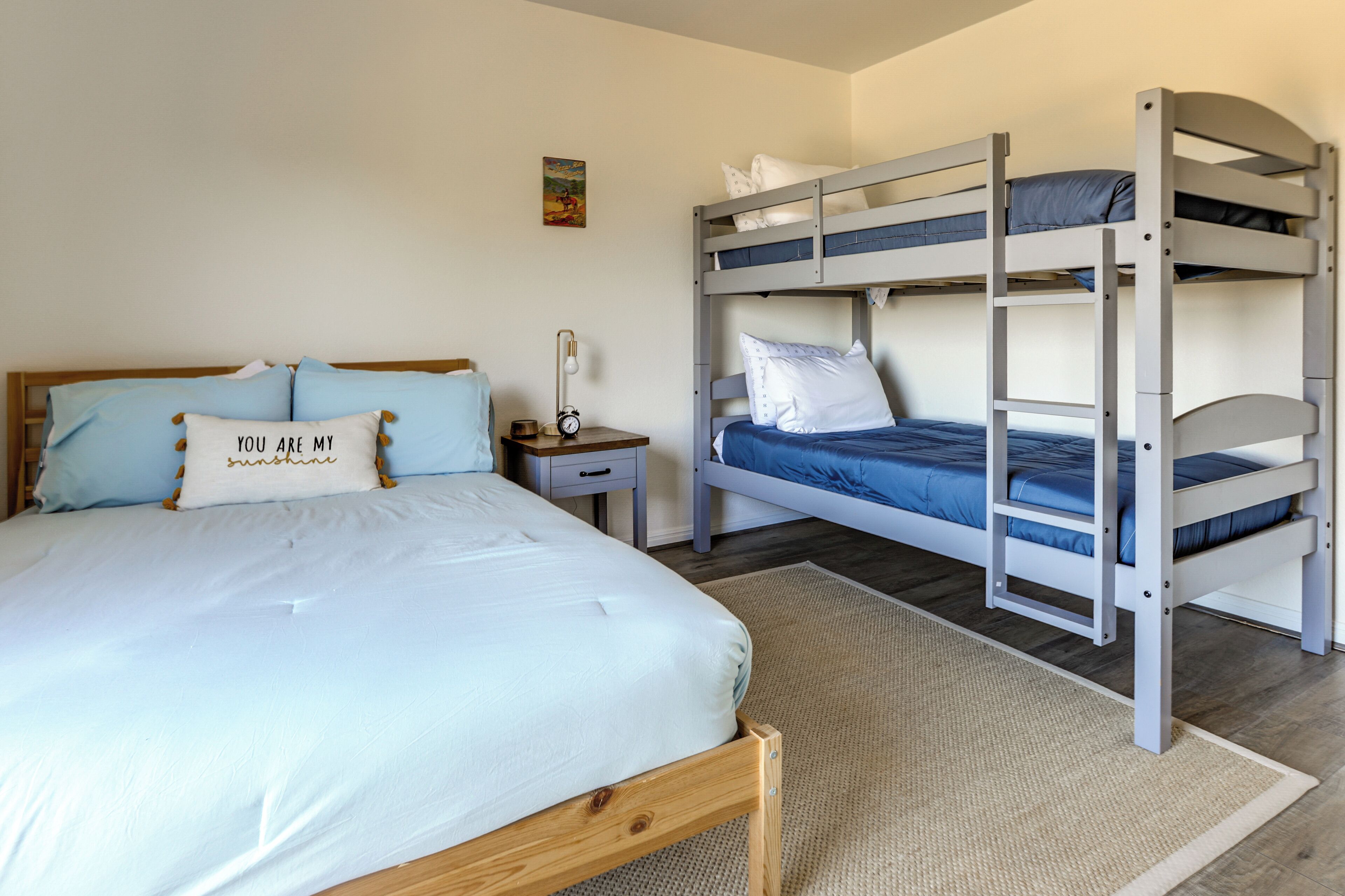 Un dormitorio con una cama individual, una mesita de noche, una lámpara y dos literas.