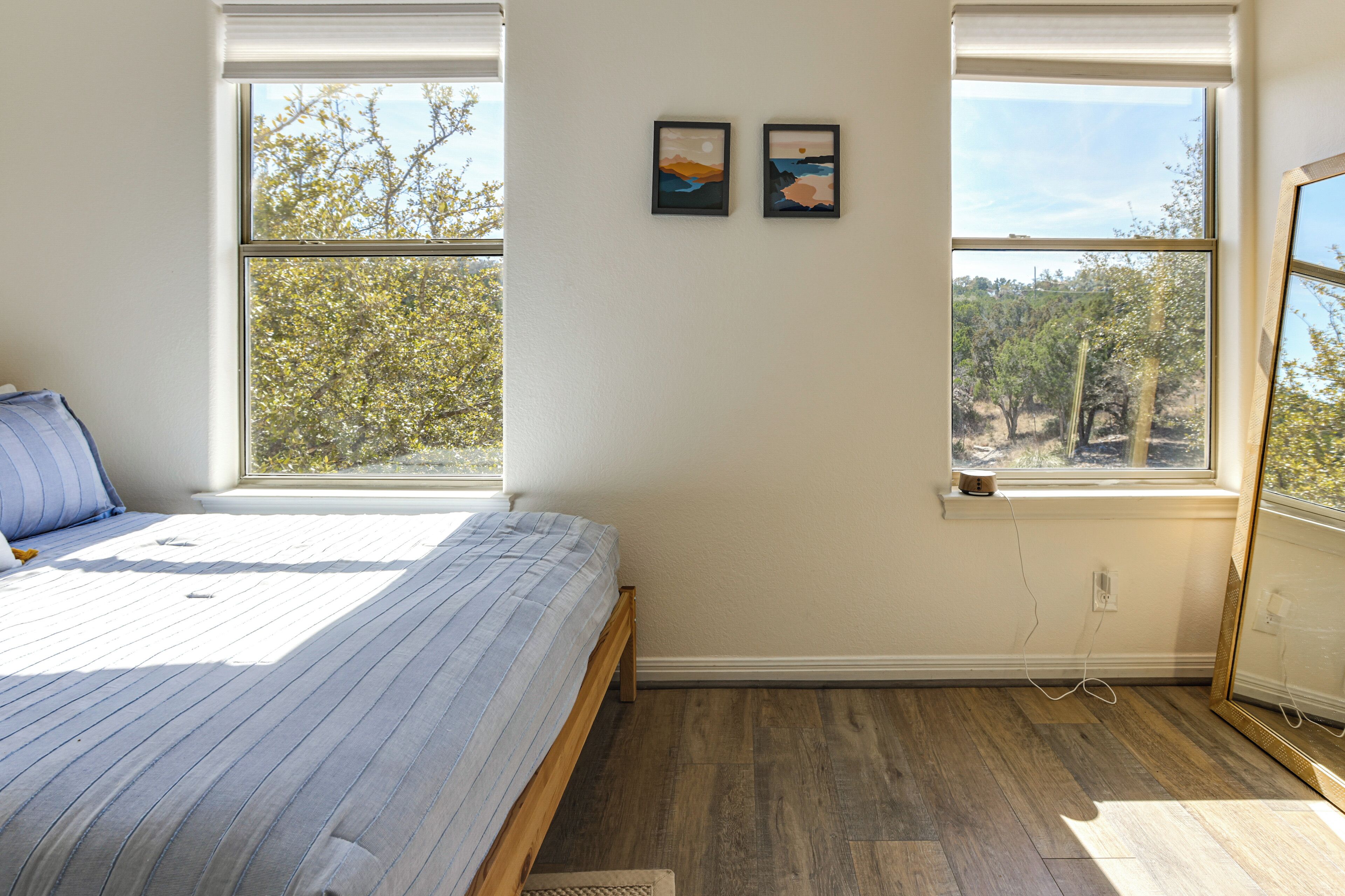 A bedroom with a bed, two windows, and a view of trees.